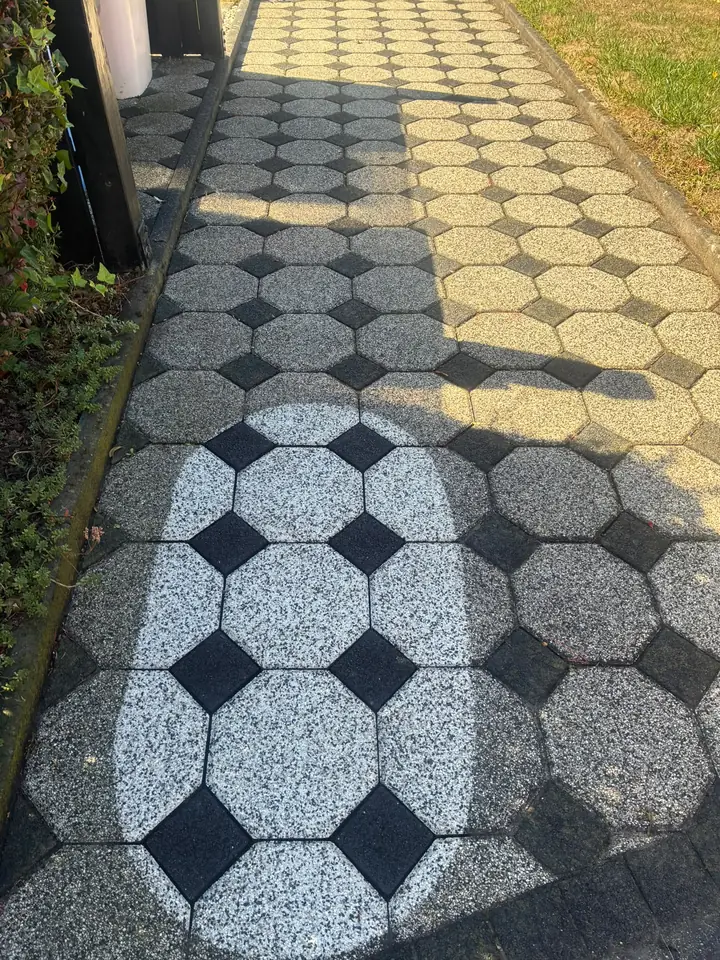 Gehweg aus Achteckplatten, in der Mitte eine gereinigte Probefläche mit hellen Platten und schwarzen Zwischensteinen, außen noch grau verschmutzt
